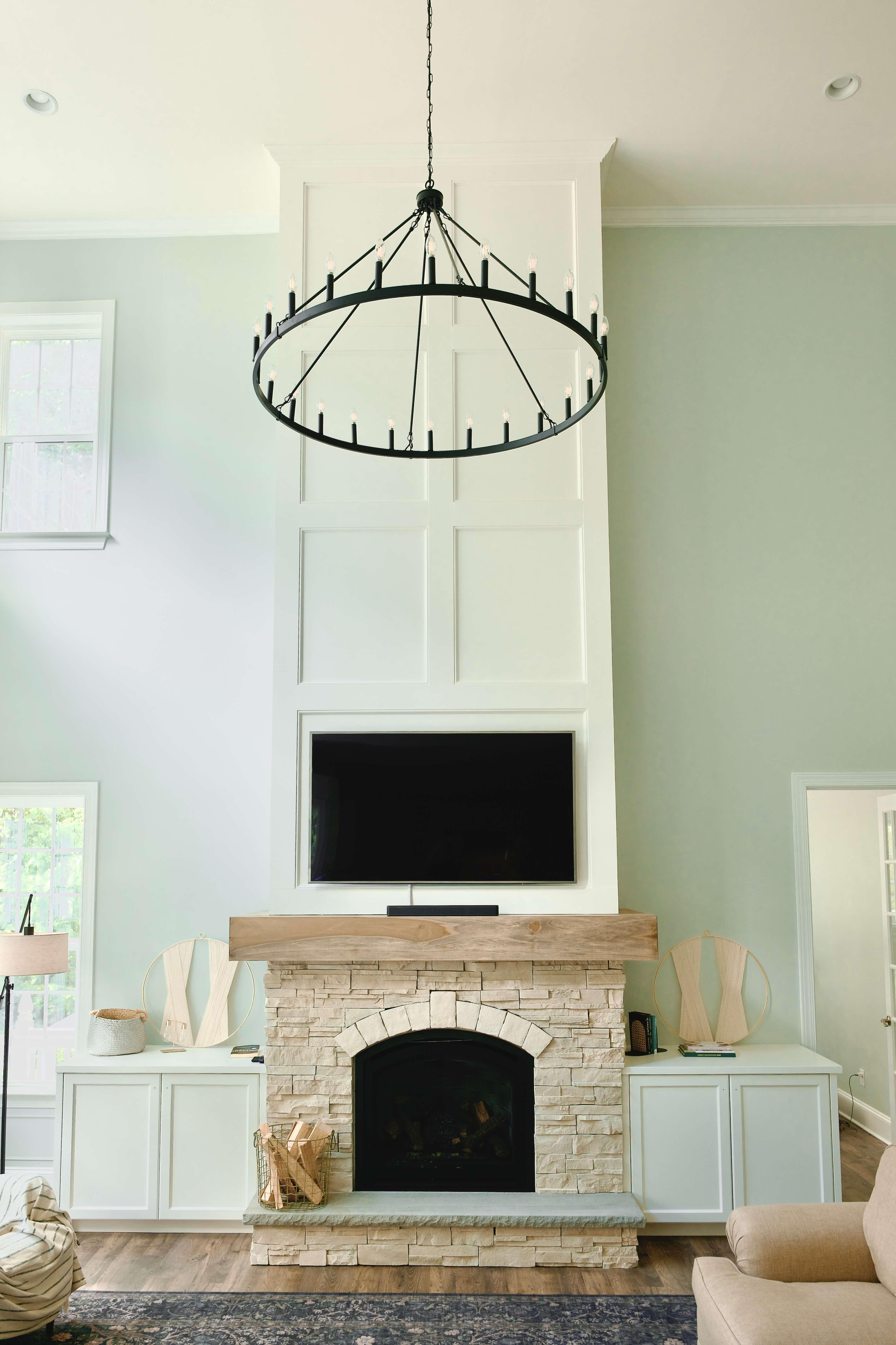 Two story stacked stone fireplace with a wood mantel, built-in cabinets and board and batten trim after a remodel