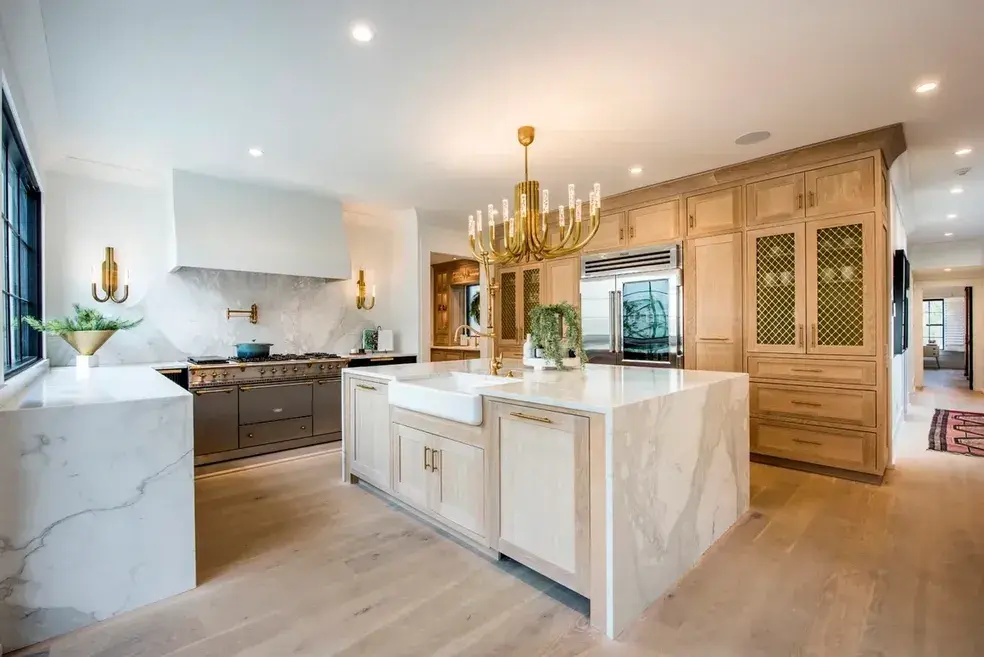 Kitchen with a marble waterfall island, white oak cabinets and a brass chandelier in a Weddington, NC home