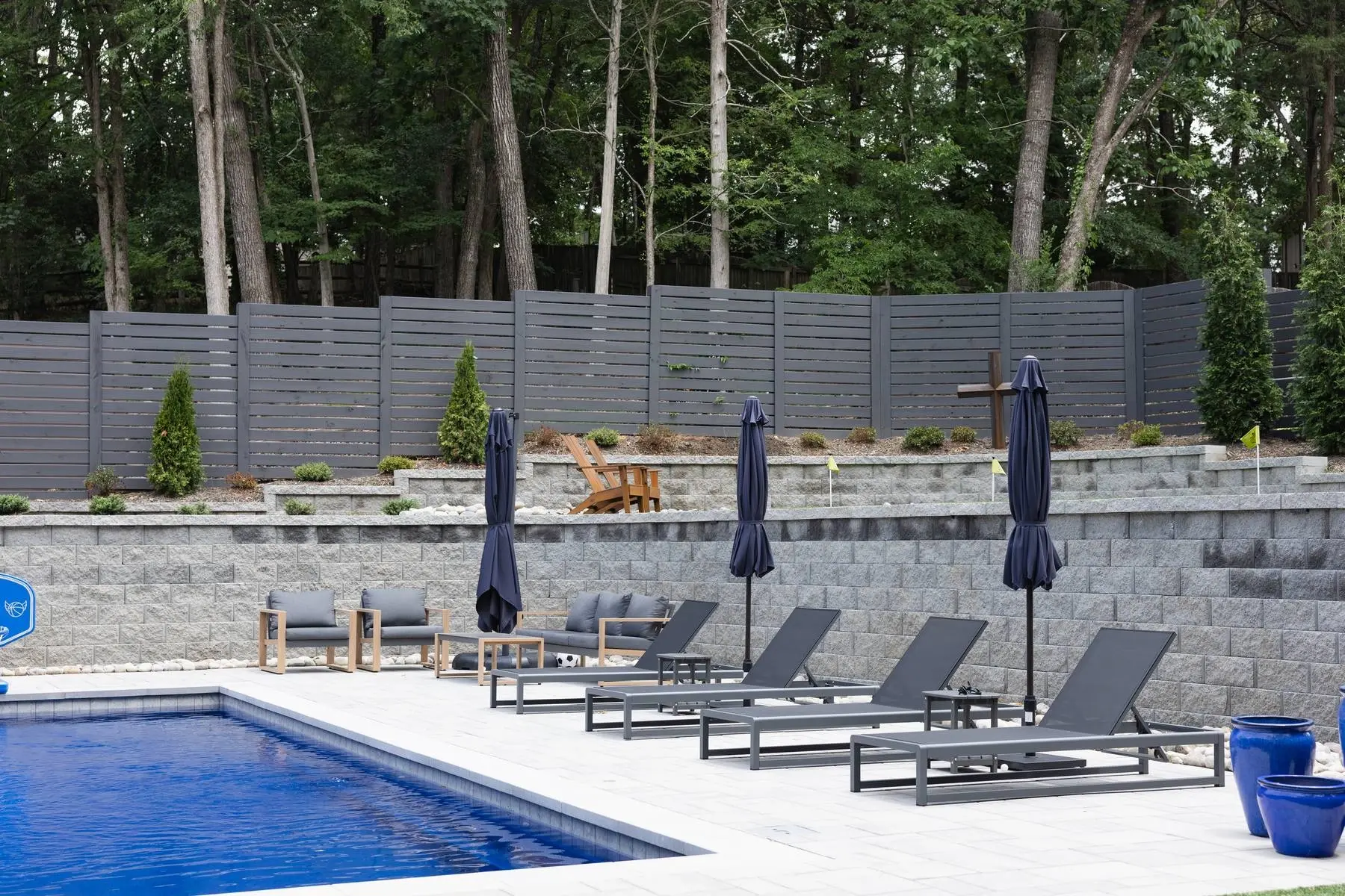 Pool deck with lounge chairs and navy umbrellas below a tiered stone retaining wall in Charlotte, NC