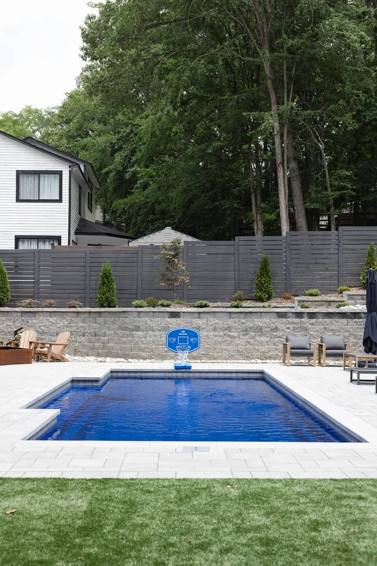 Backyard pool with a basketball hoop, paver deck and stacked stone retaining wall in Charlotte, NC