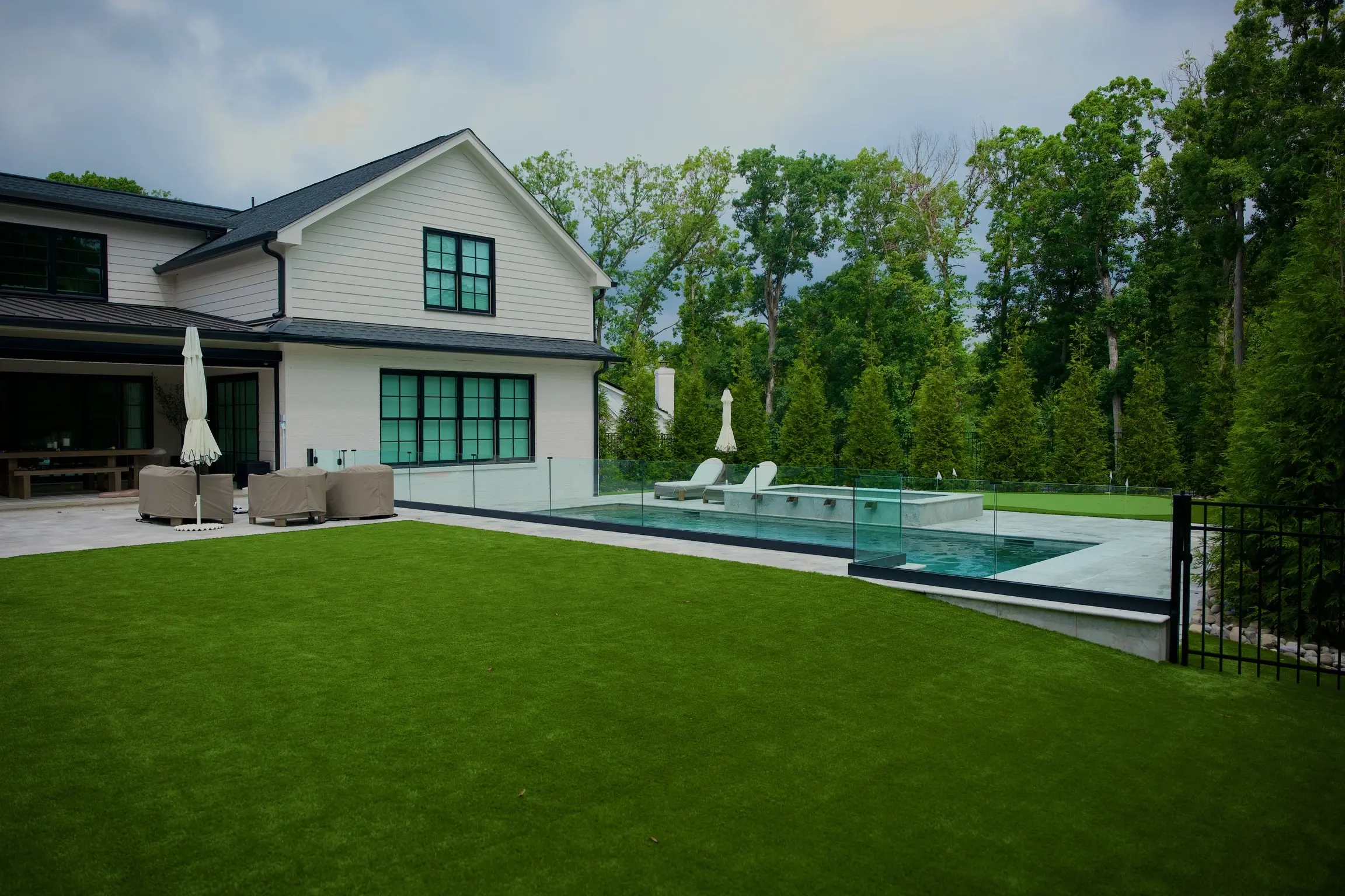 Inground pool with glass fencing and a turf lawn behind a white modern farmhouse in Charlotte, NC