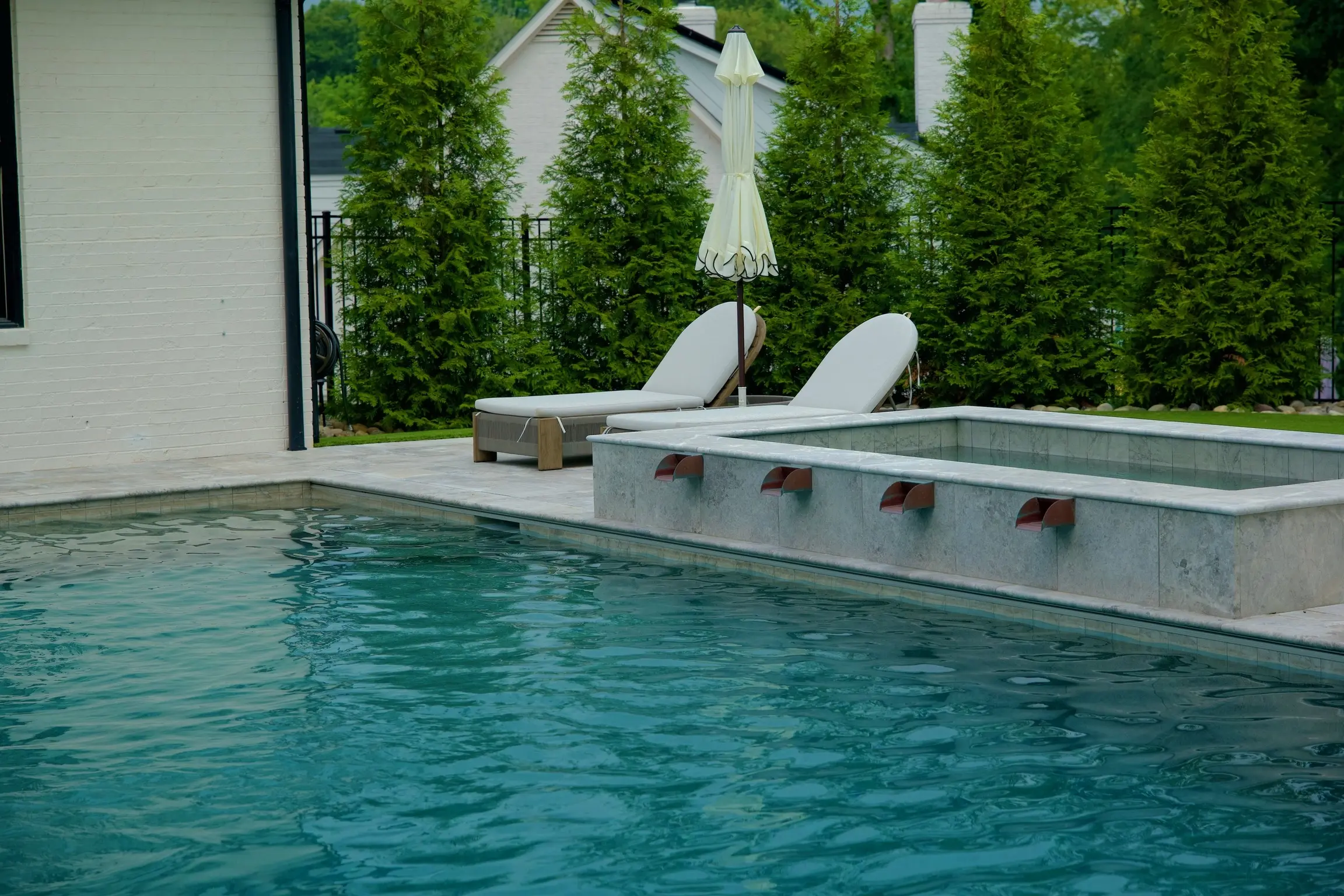 Raised spa with copper scupper spillways next to a pool and lounge chairs at a Charlotte, NC home
