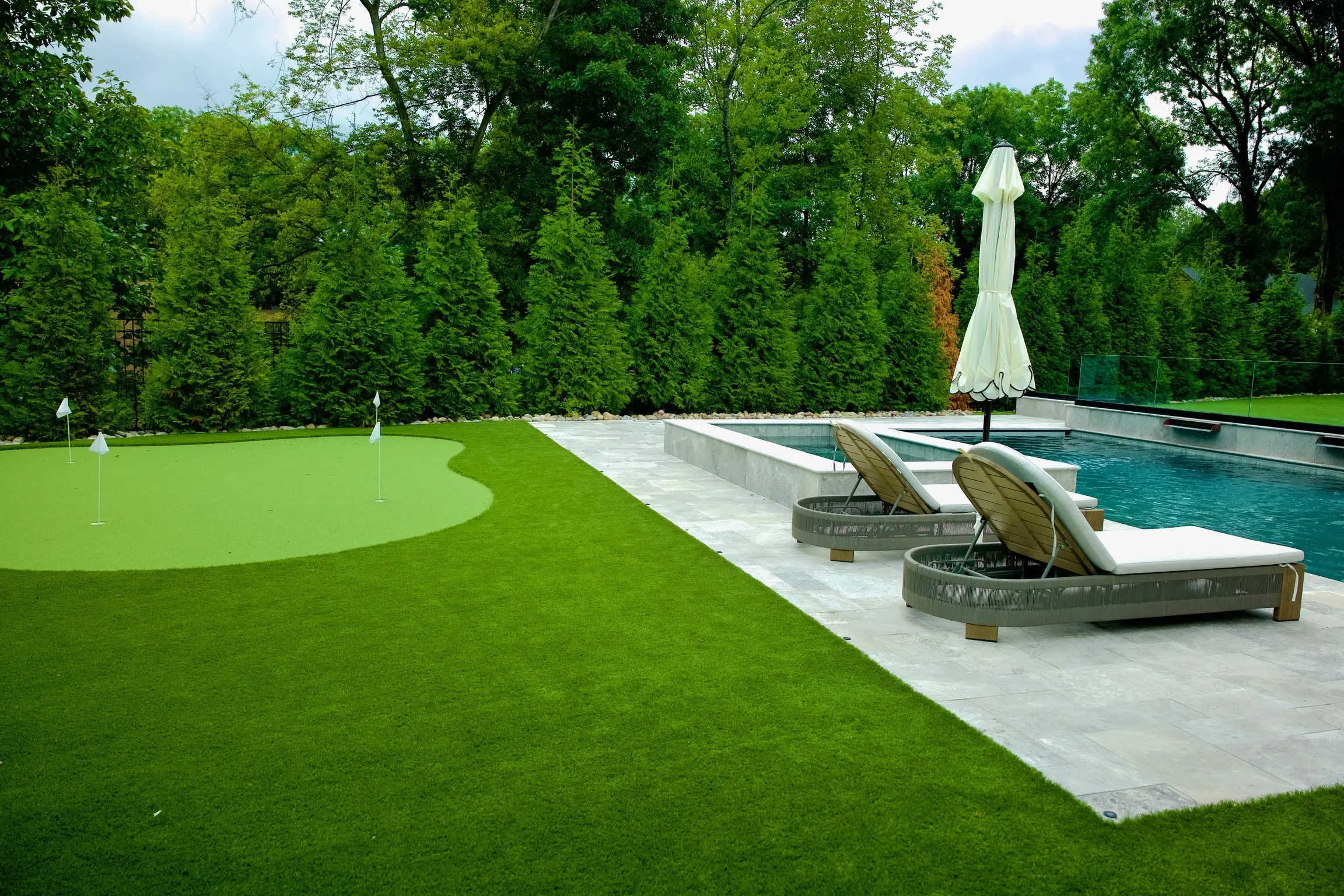 Backyard putting green next to a pool with lounge chairs and evergreen privacy trees in Charlotte, NC