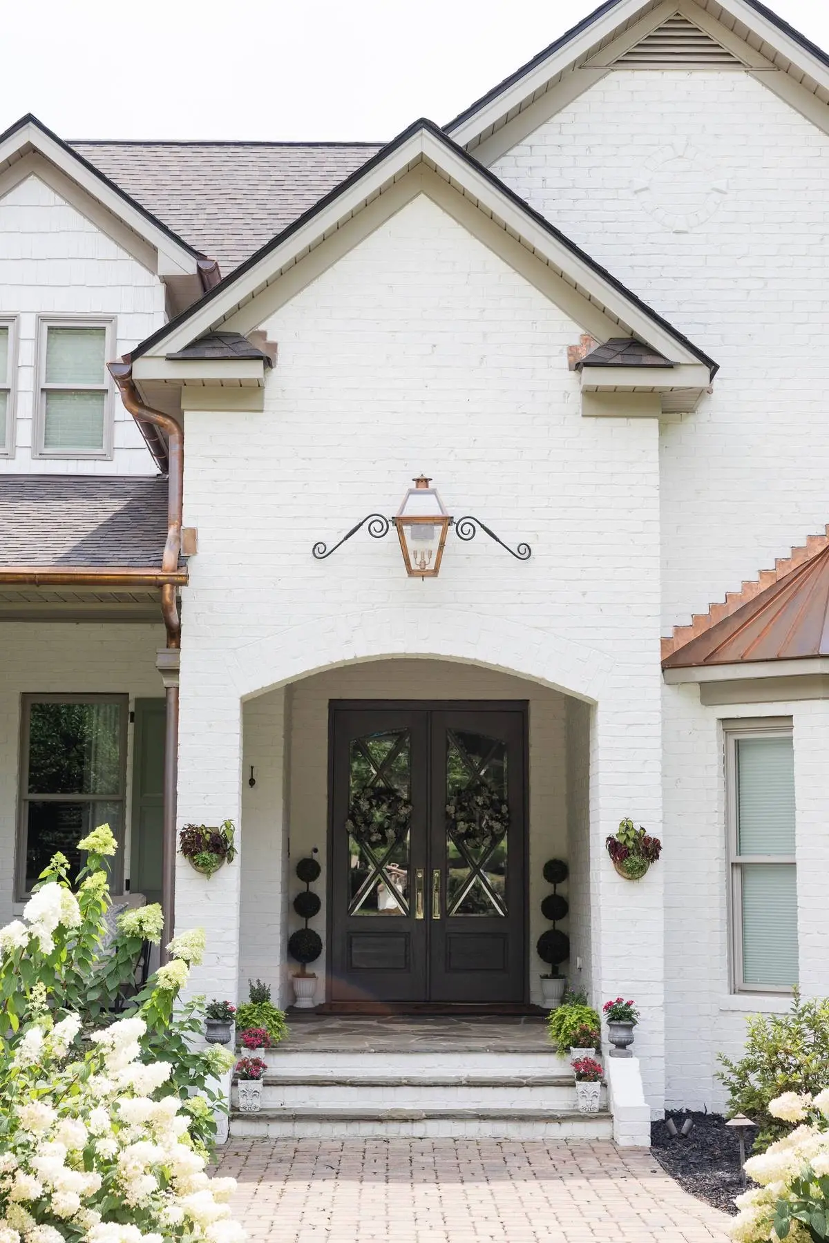 Arched front entry of a white brick home in Weddington, NC with a gas lantern and new copper gutters