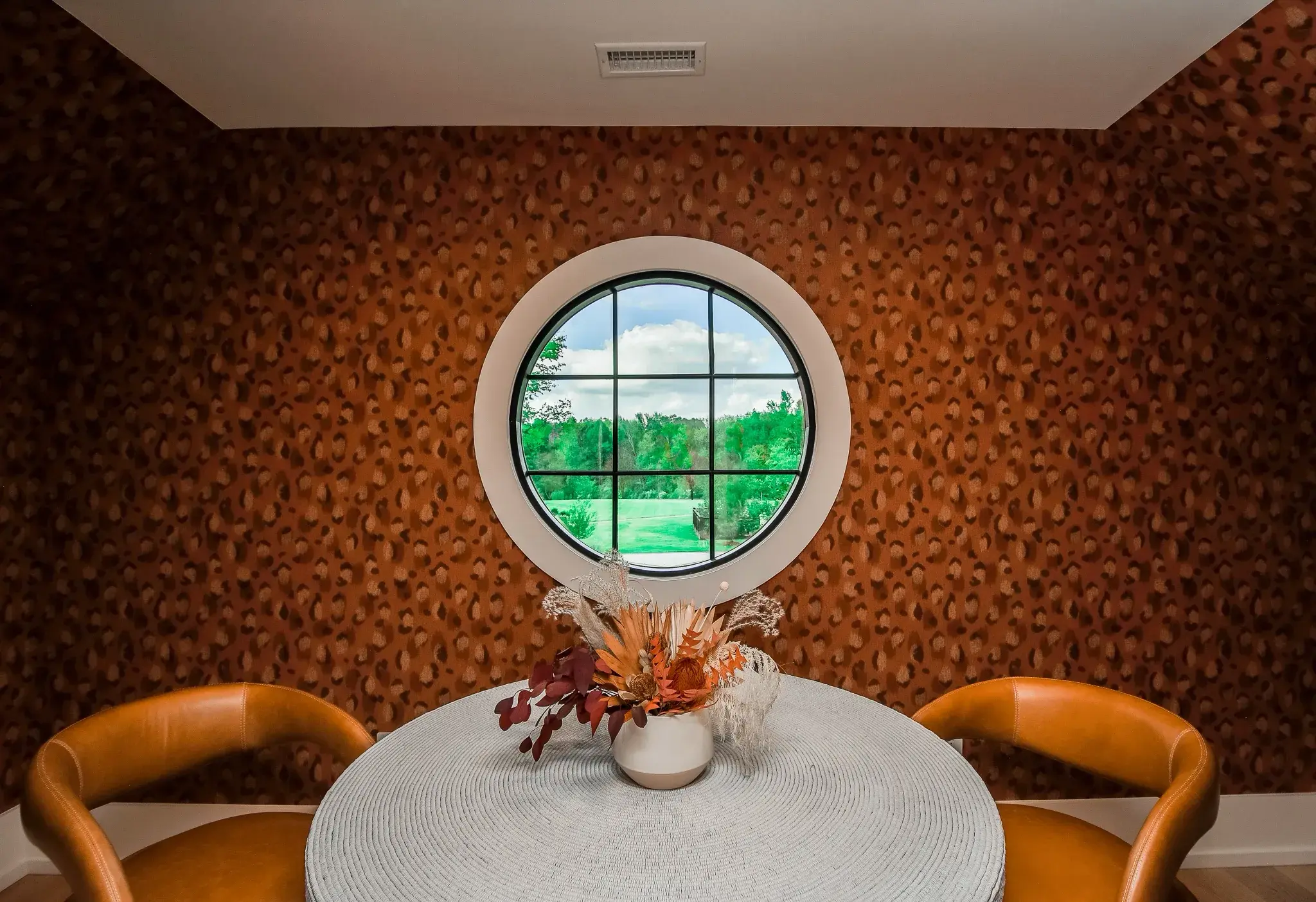Breakfast nook with a round porthole window, terracotta textured walls, a round table and leather chairs