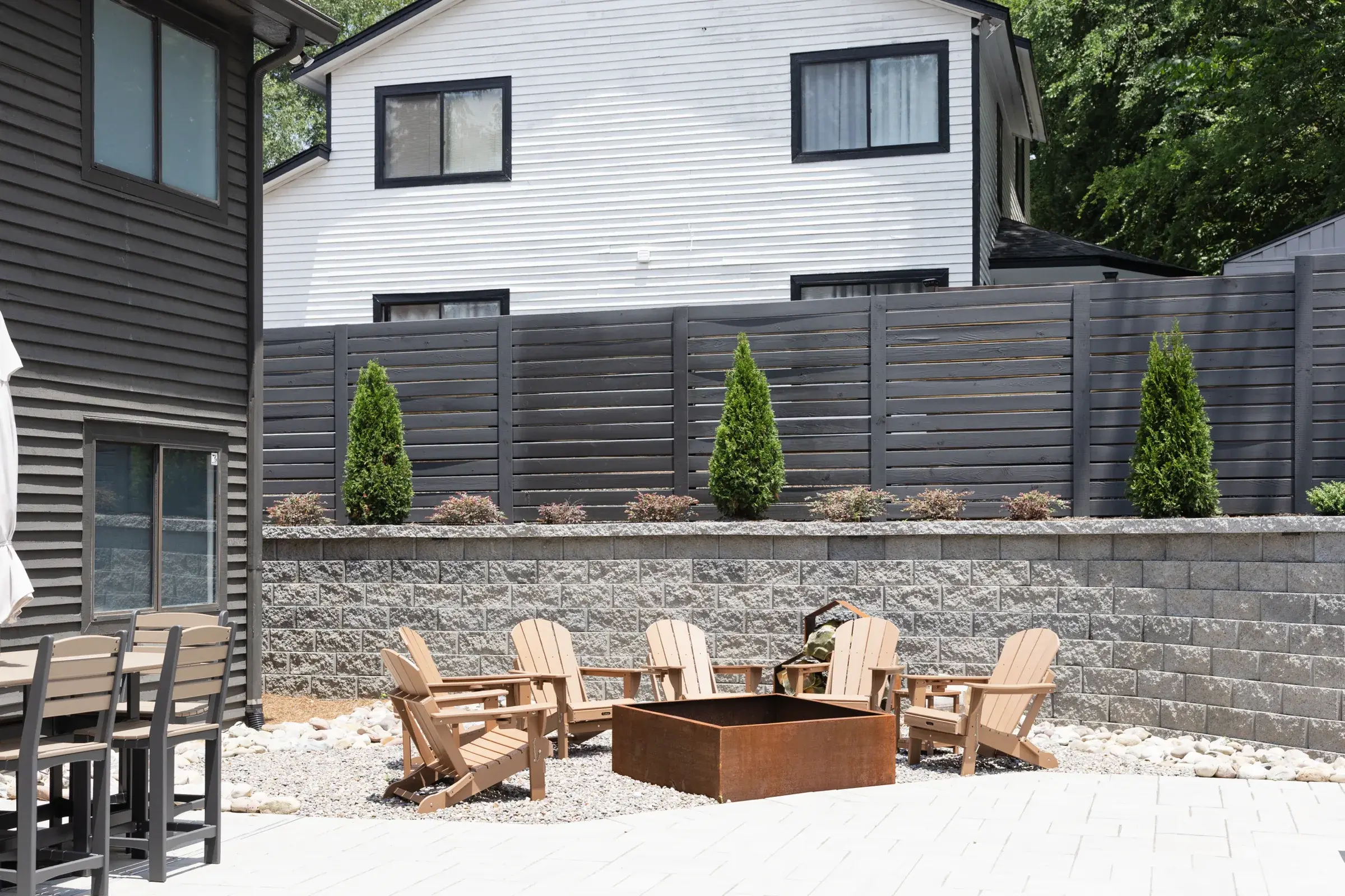 Paver patio with Adirondack chairs around a steel fire pit below a stacked stone retaining wall in Charlotte, NC