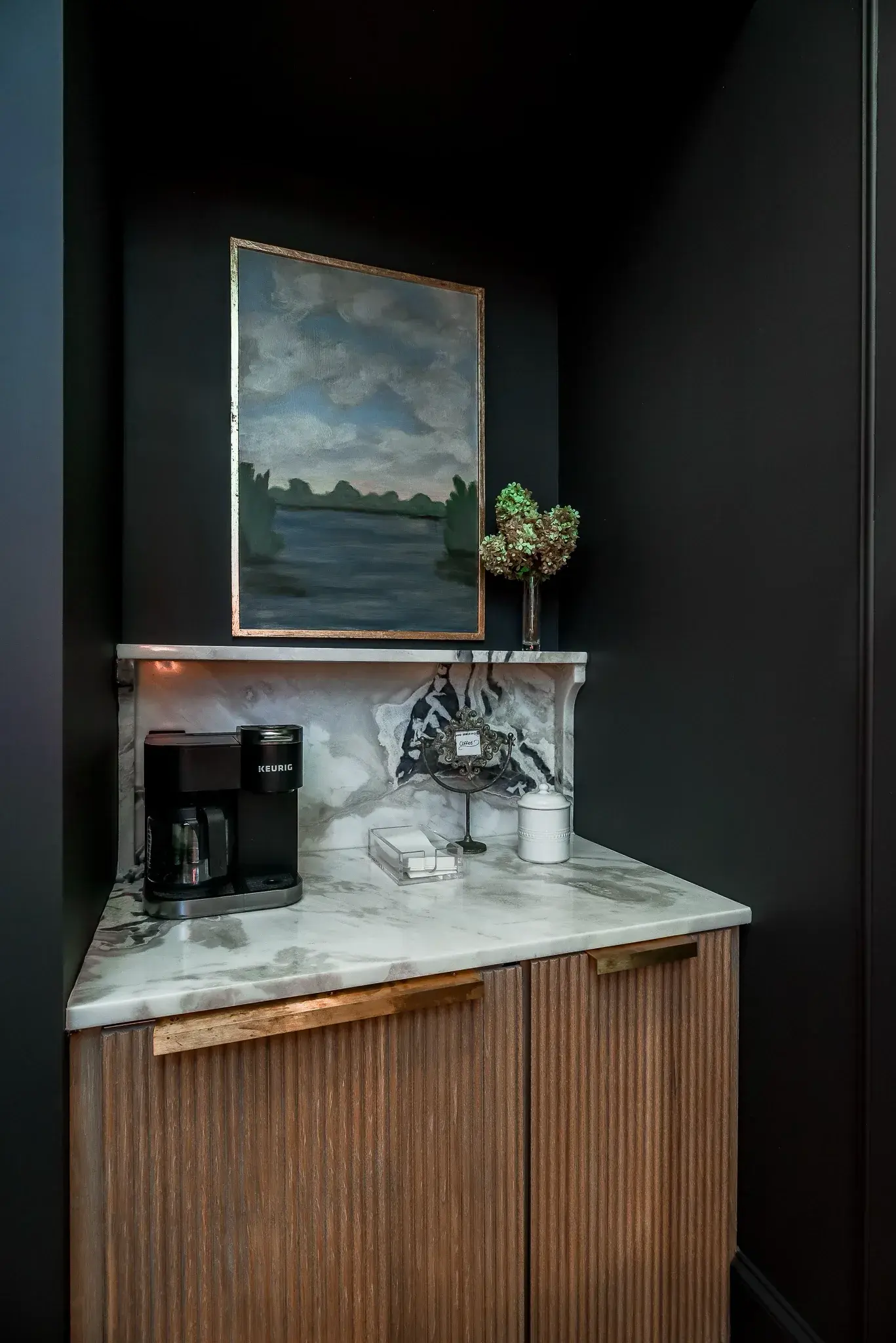 Coffee bar niche with a marble counter and carved shelf, a fluted wood cabinet and dark painted walls