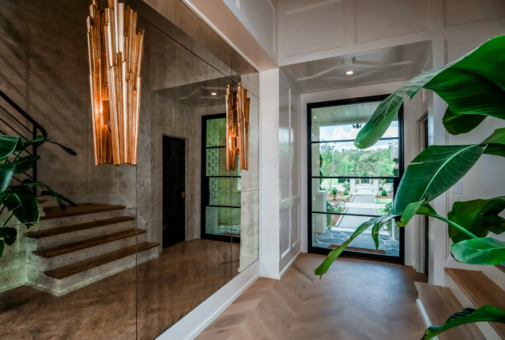 Entry with a herringbone wood floor, a tall brass sconce, a black steel front door and an open stair