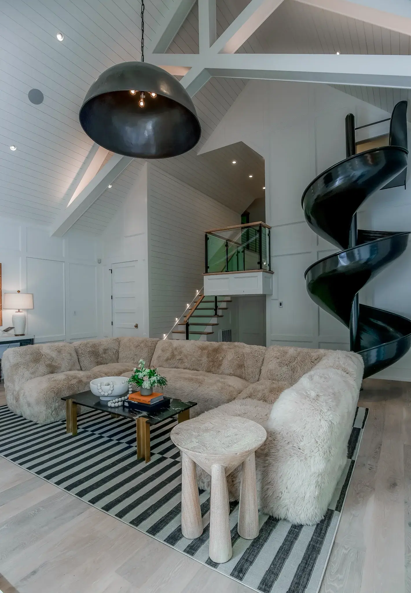 Great room with a vaulted shiplap ceiling, a curved sectional, a dome pendant and a black spiral slide from the loft