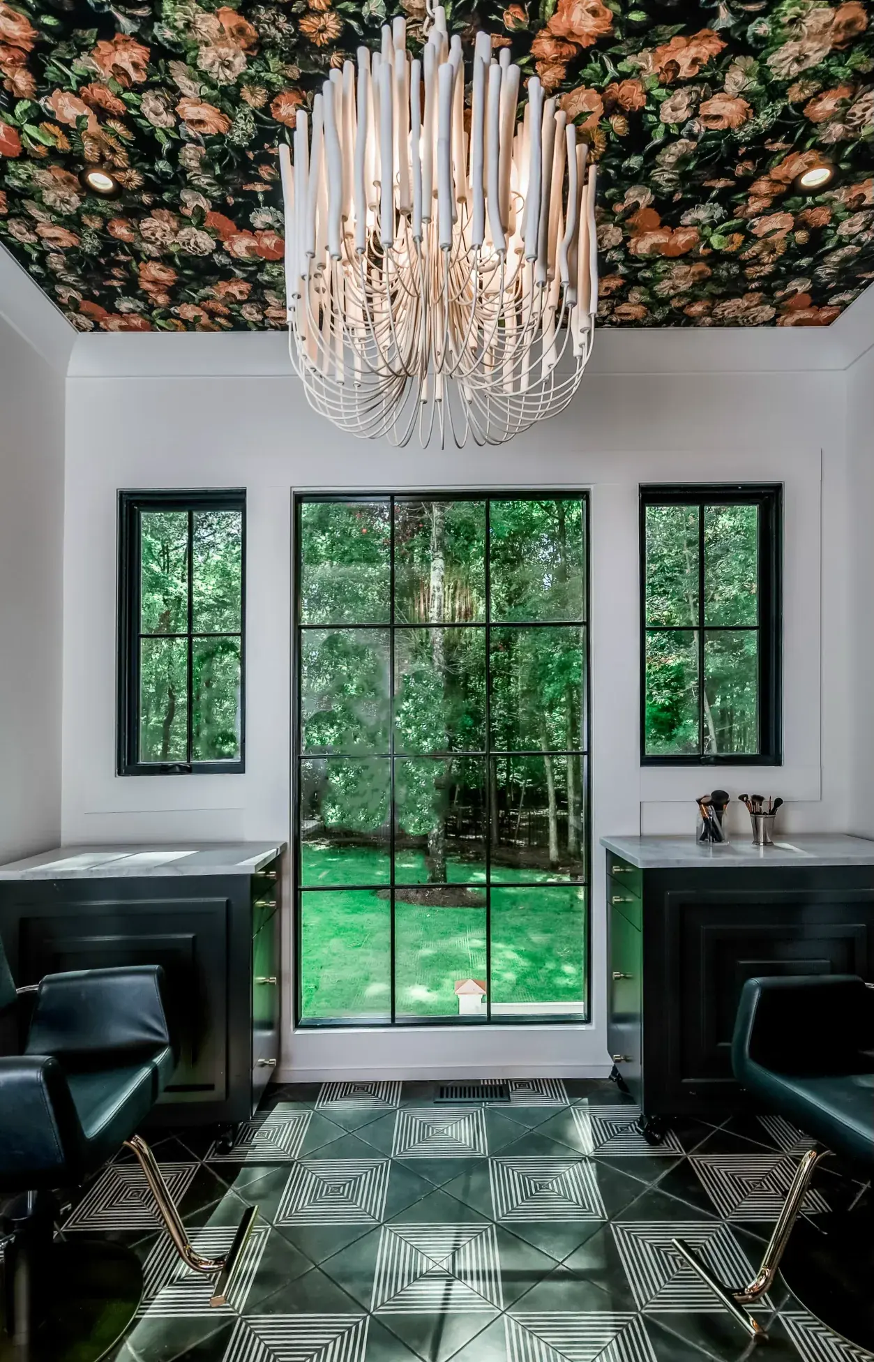 Home salon with a tall black steel window, a chandelier and matching black vanities on patterned tile