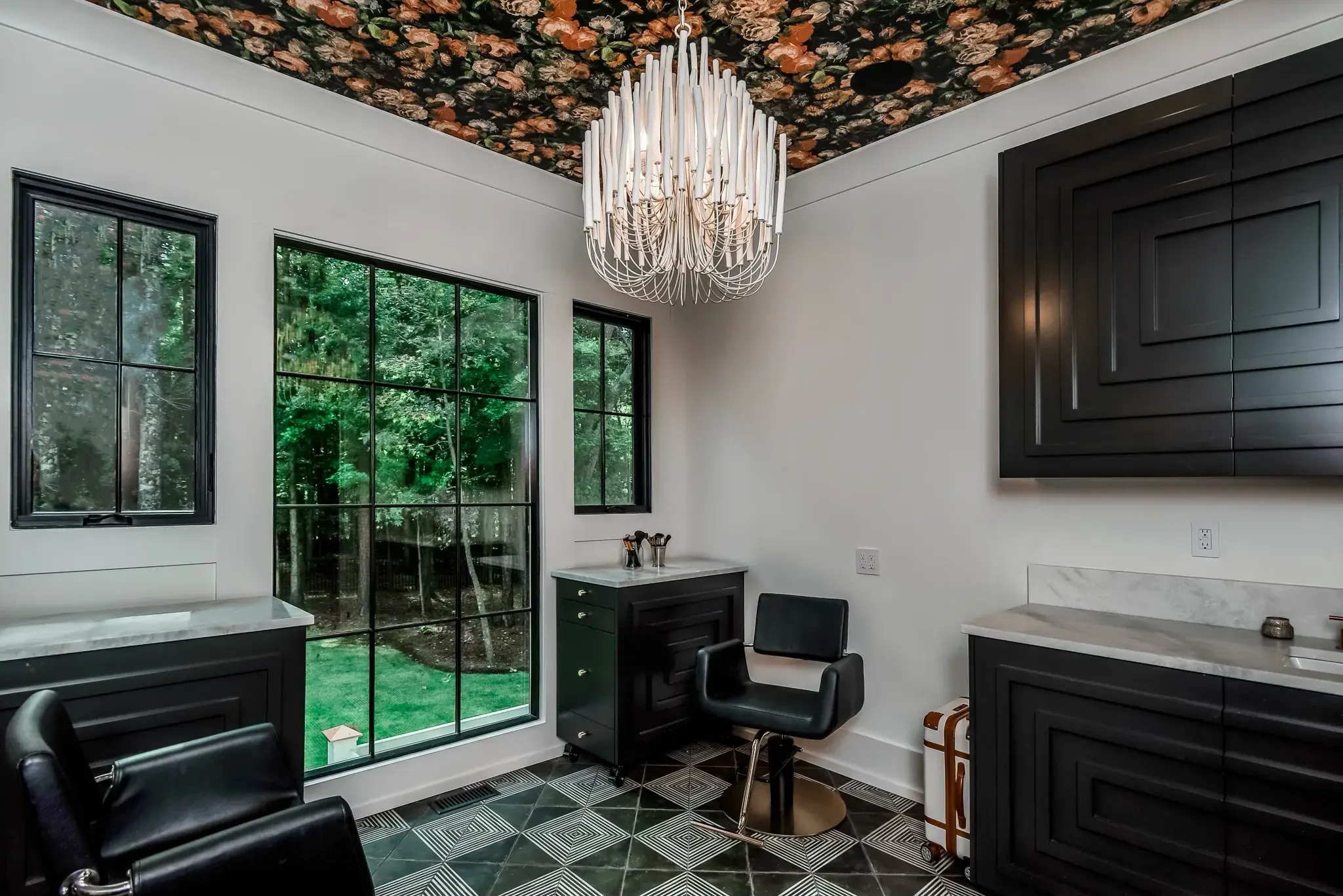 Home salon with a floral papered ceiling, a crystal chandelier, black cabinets and marble counters