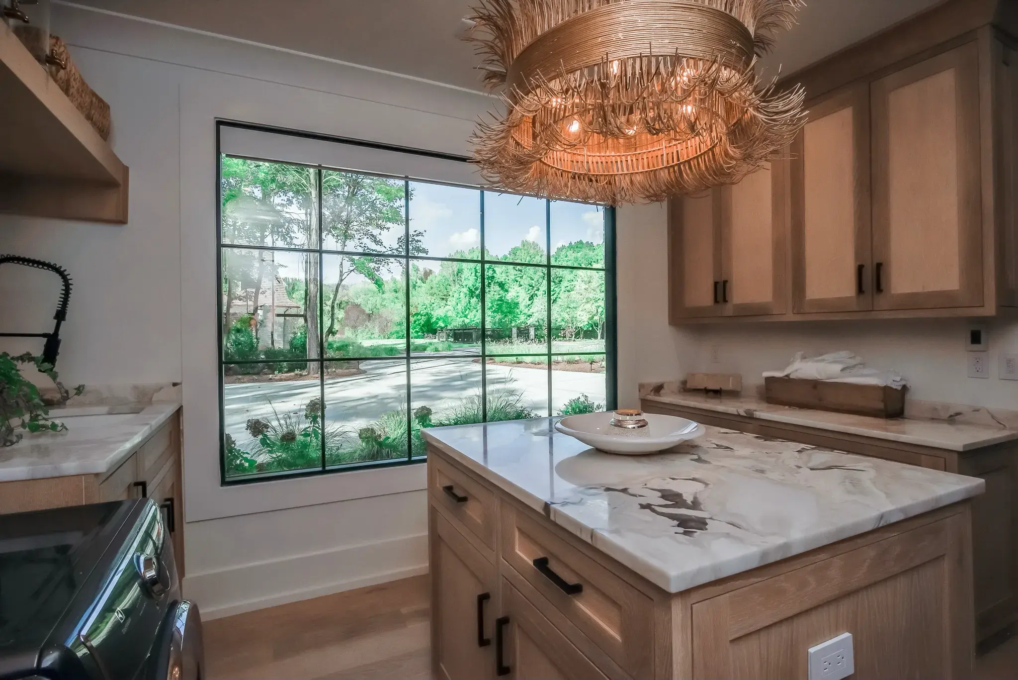 Laundry room with white oak cabinets, a marble topped island, a woven chandelier and a green steel window