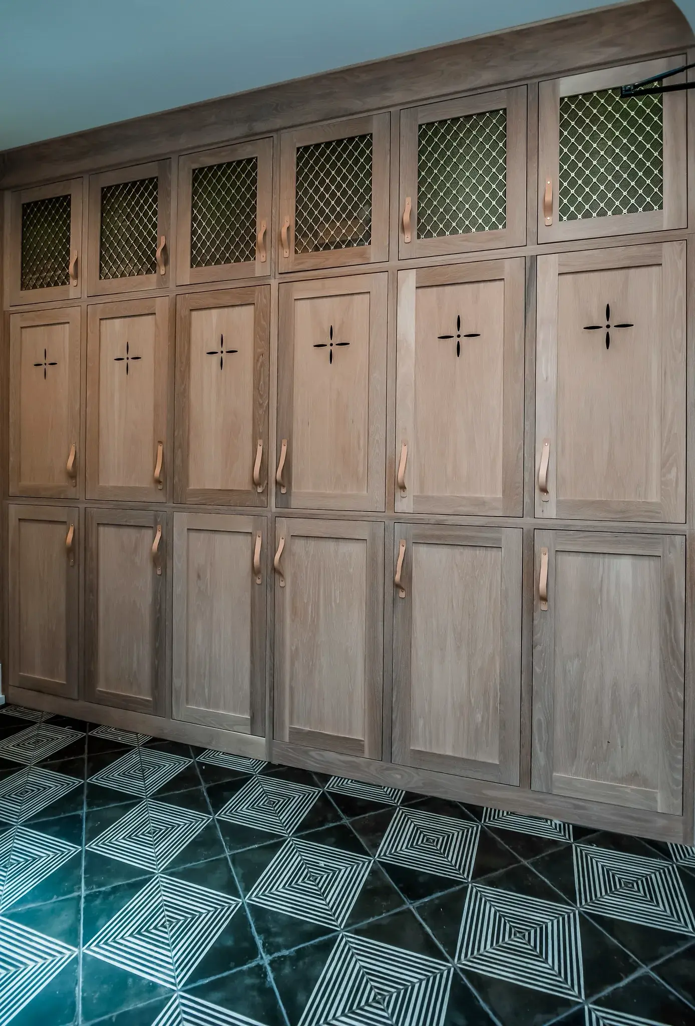 Custom white oak mudroom lockers with brass mesh panels, leather pulls and a patterned green tile floor