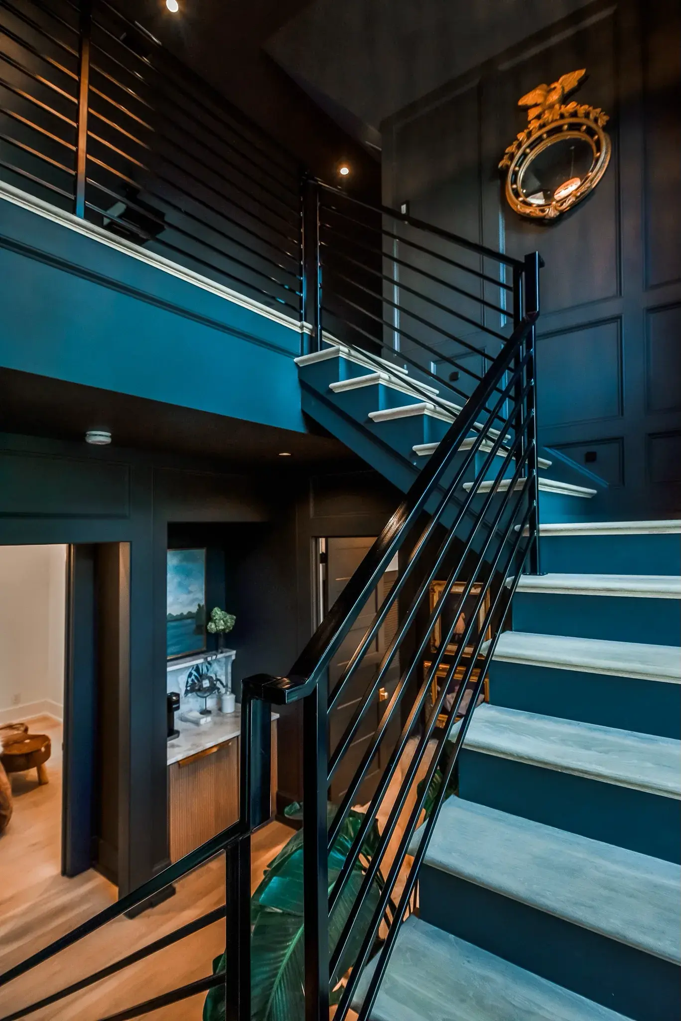Two story navy stairwell with a black metal railing, paneled walls and lit stair treads