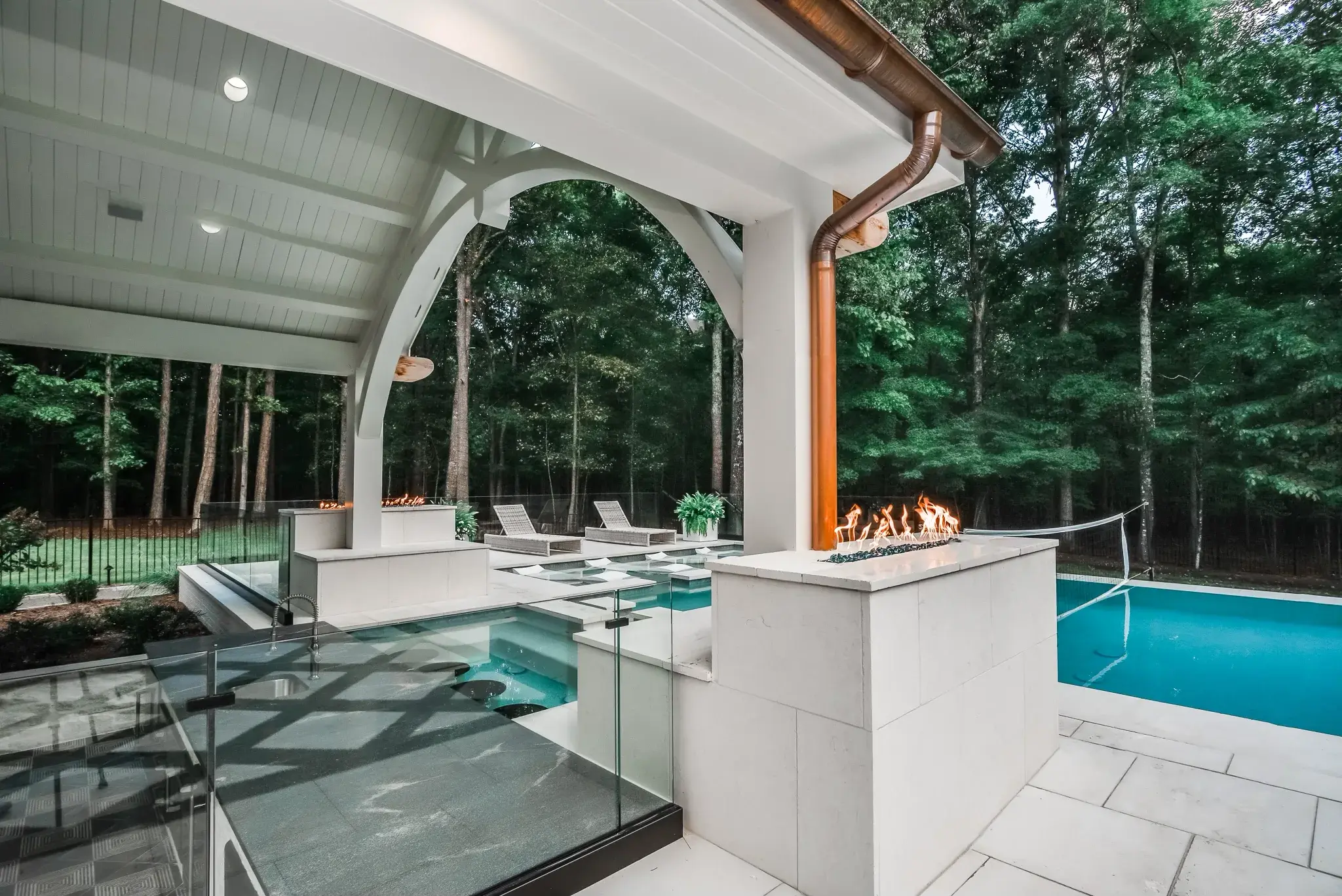 Poolside pavilion with a timber arch, a linear gas fire feature, glass railing and a copper downspout