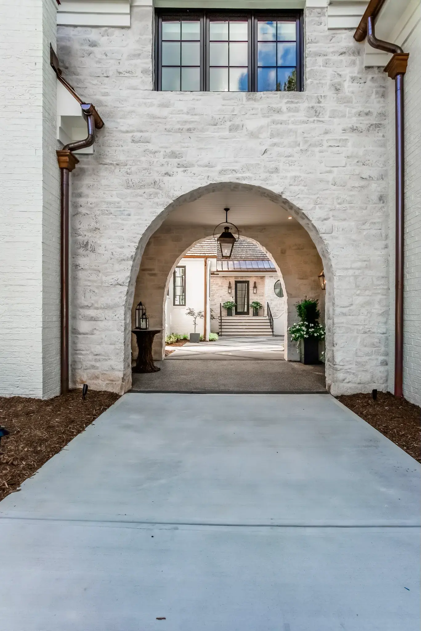 White painted brick porte cochere with an arched opening and copper downspouts leading to the front entry