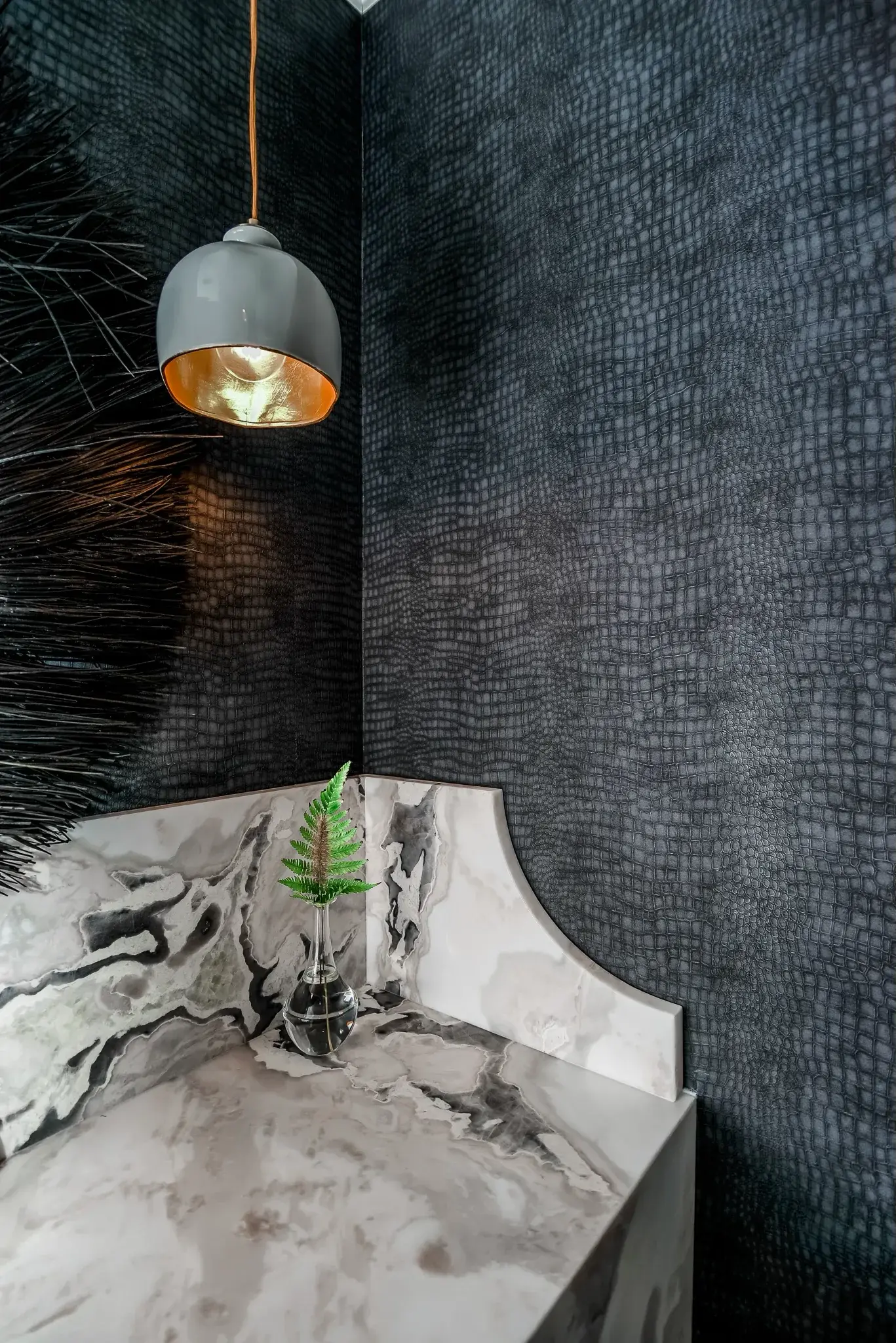 Close view of a curved marble vanity edge and a brass lined pendant against dark textured wallpaper