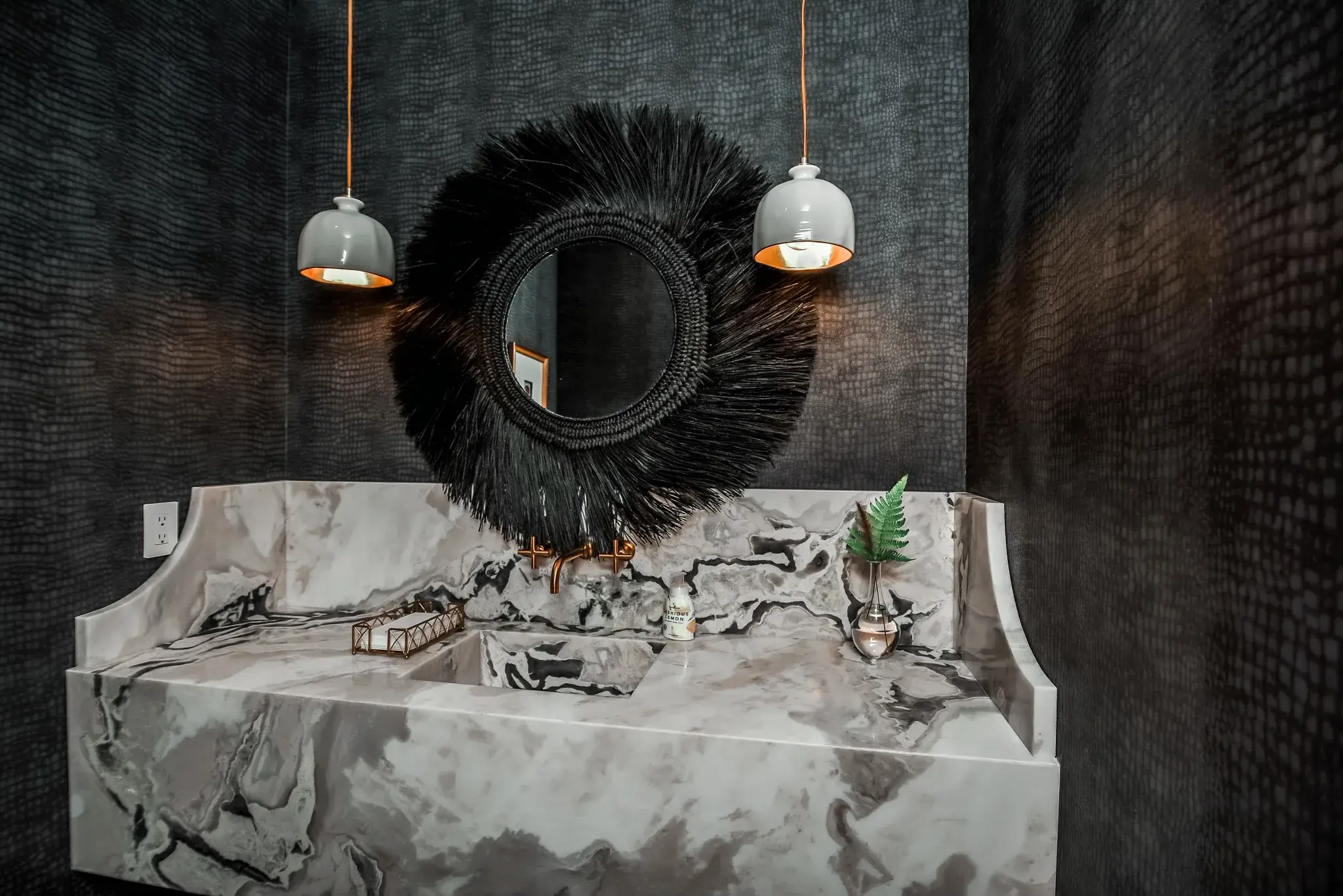 Powder room with a curved marble vanity, a black feather mirror and two dome pendants on textured wallpaper