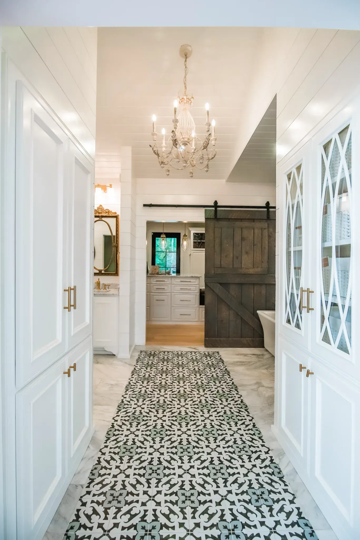 Primary bath hallway with a shiplap ceiling, crystal chandelier, sliding barn door and patterned tile floor