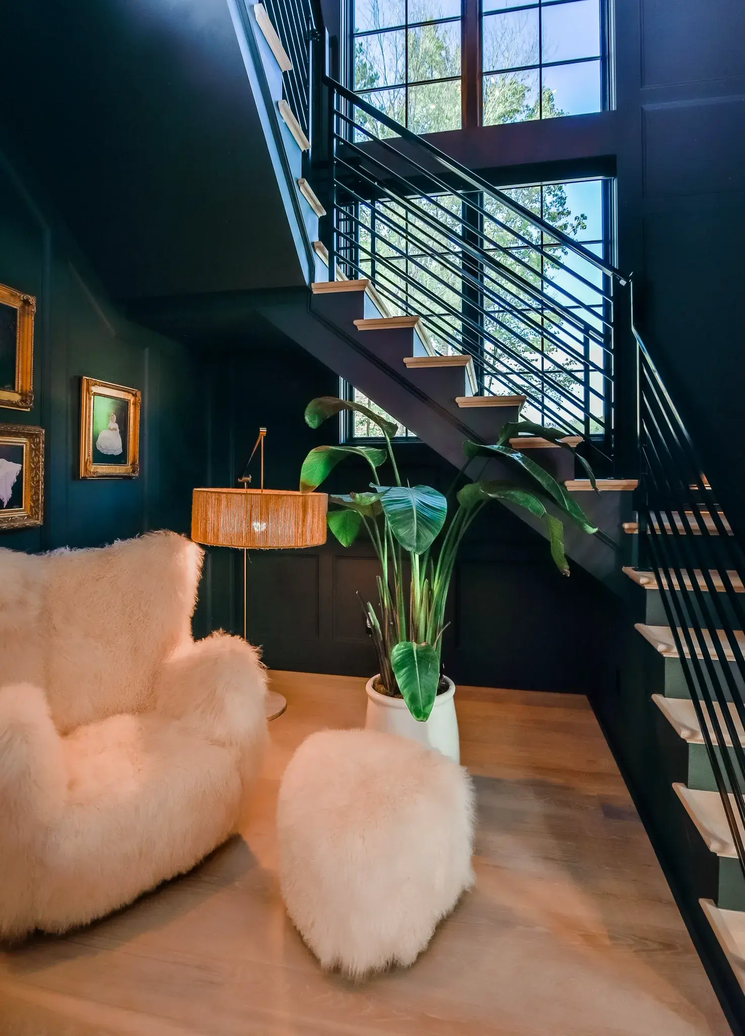 Sitting nook under an open stair with dark green walls, sheepskin chairs and framed art