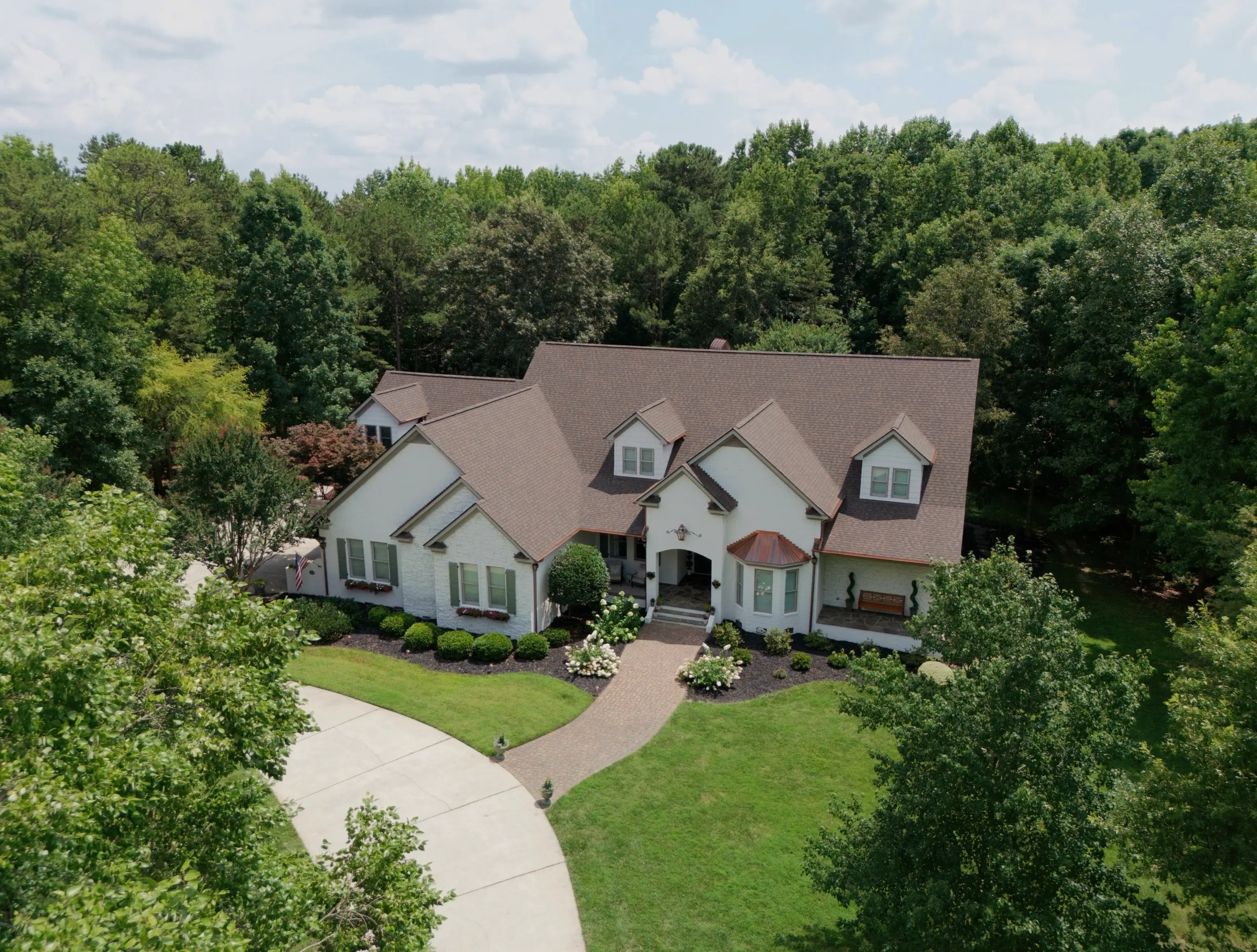 Aerial view of a white brick home with a circular driveway on a wooded lot in Weddington, NC