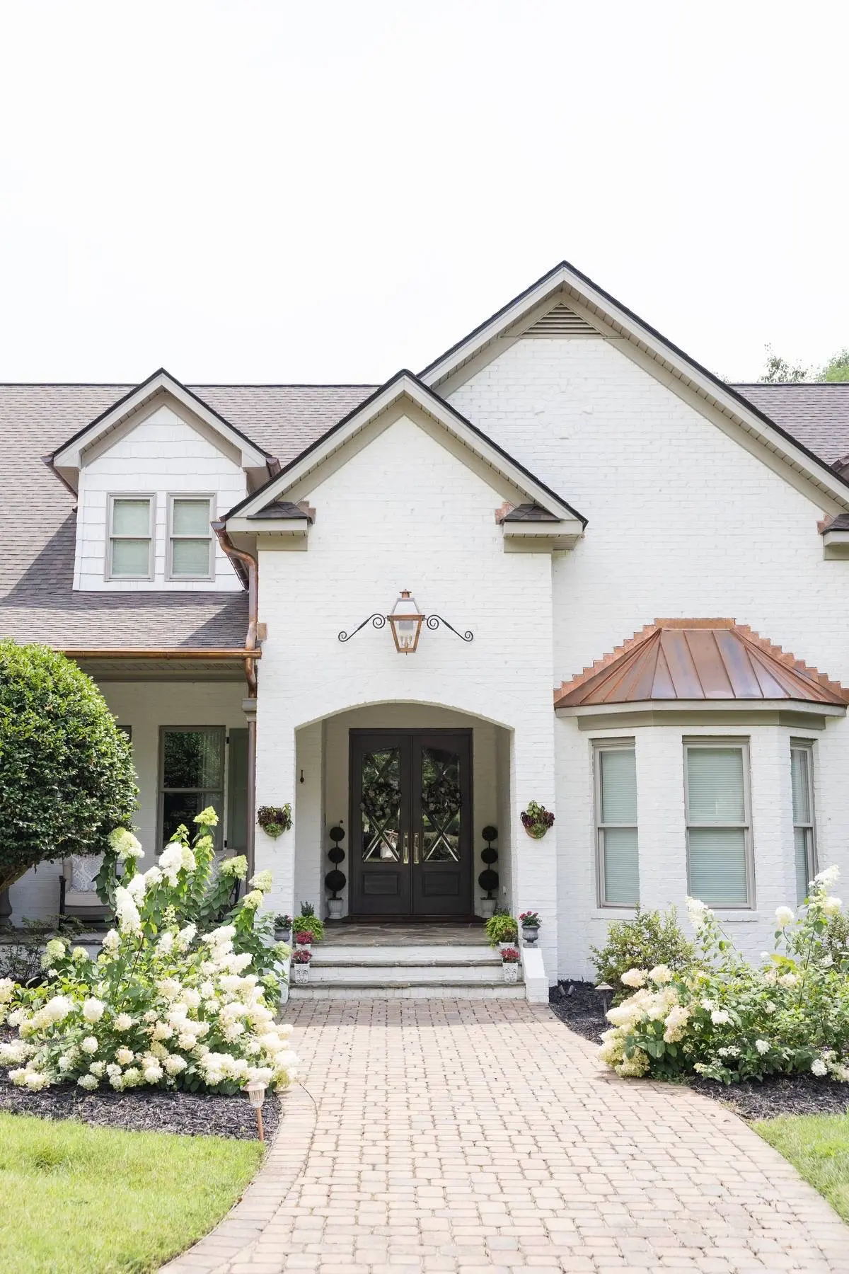 Arched front entry of a white brick home in Weddington, NC with a copper bay window roof