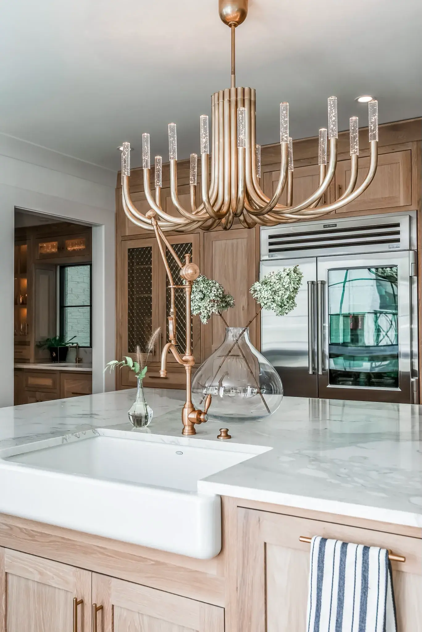 White oak kitchen with a farmhouse apron sink, marble counters and a fluted brass chandelier